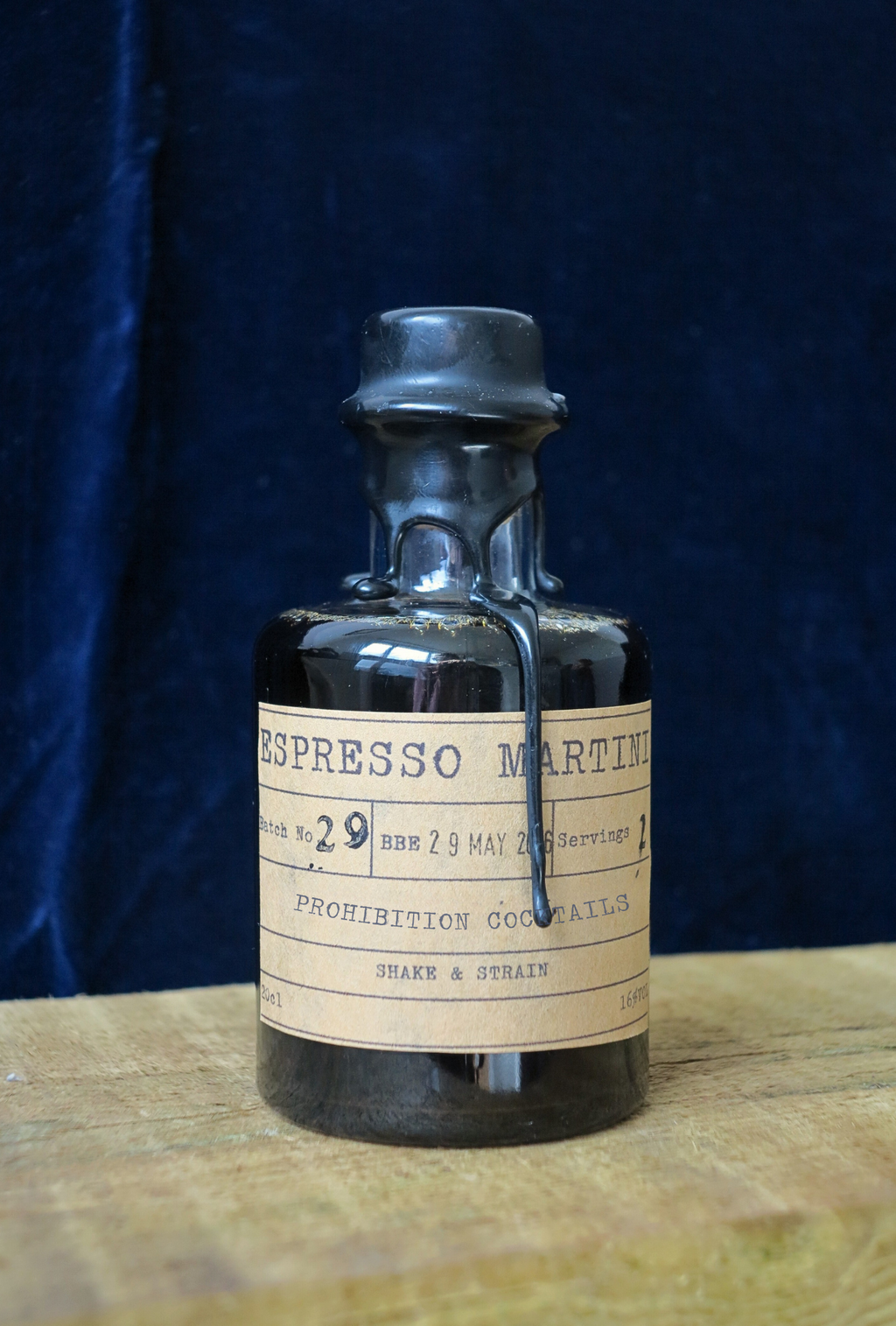 Vintage-style bottle with a label 'Espresso Martini' by 'Prohibition Cocktails' on a wooden surface and dark blue background.