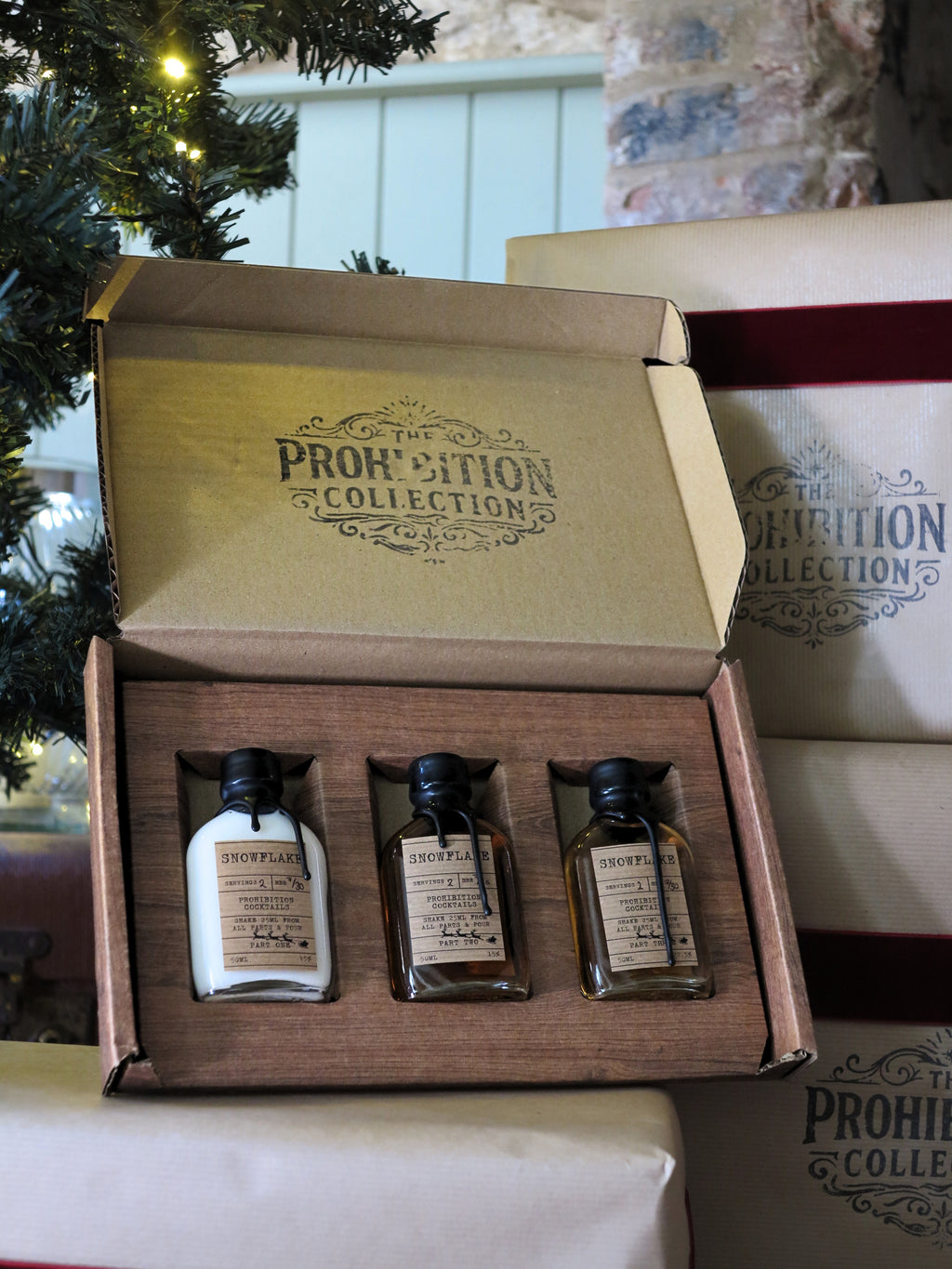 An open gift box from The Prohibition Collection containing three small bottles, shown with other branded boxes in the background.